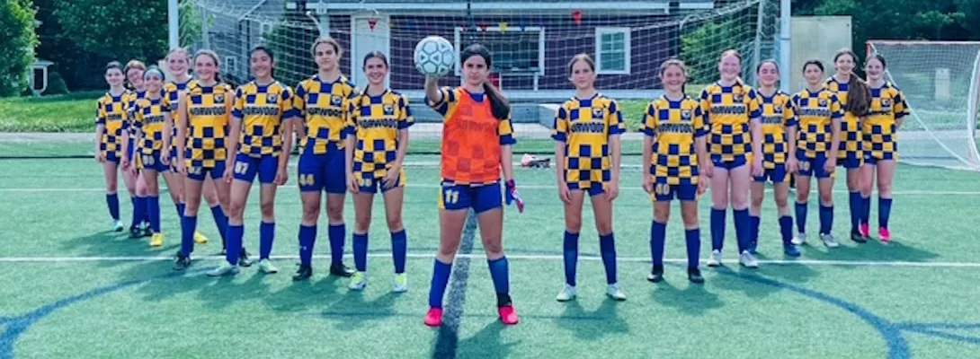 Norwood girls youth soccer team lined up crossing arms, with the goalie in the middle holding a soccer ball