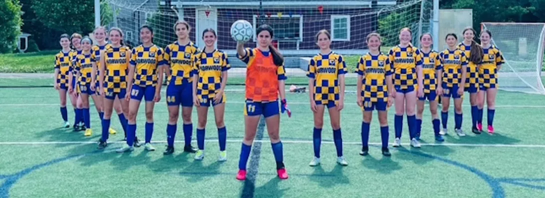 Norwood girls youth soccer team lined up crossing arms, with the goalie in the middle holding a soccer ball